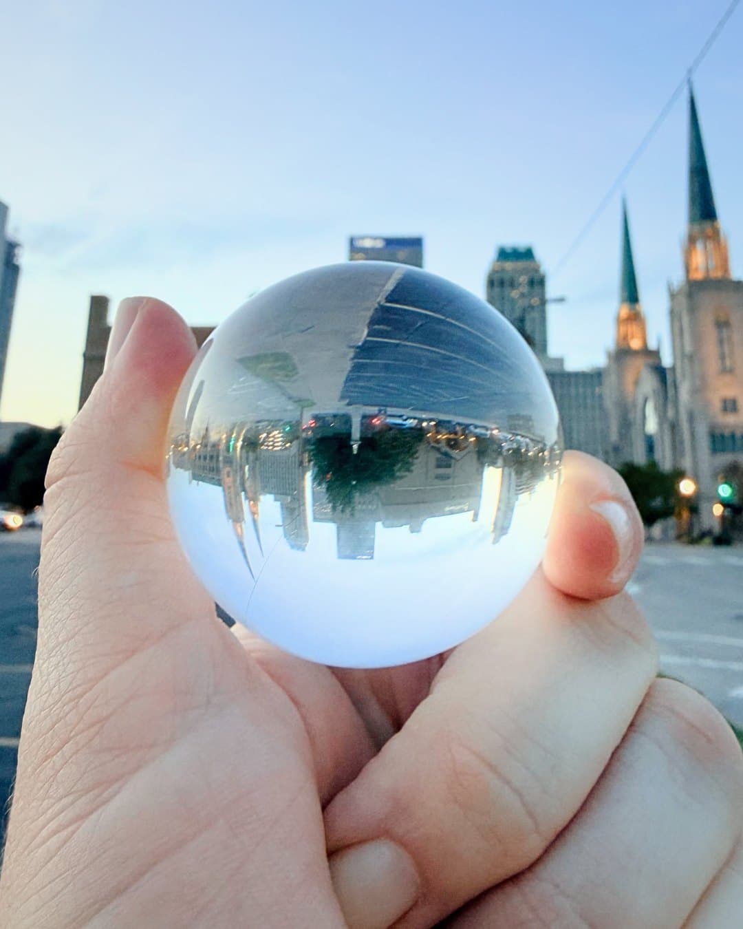 A glass sphere held up to downtown Tulsa at dusk, the skyline and Boston Avenue spires reflected in it
